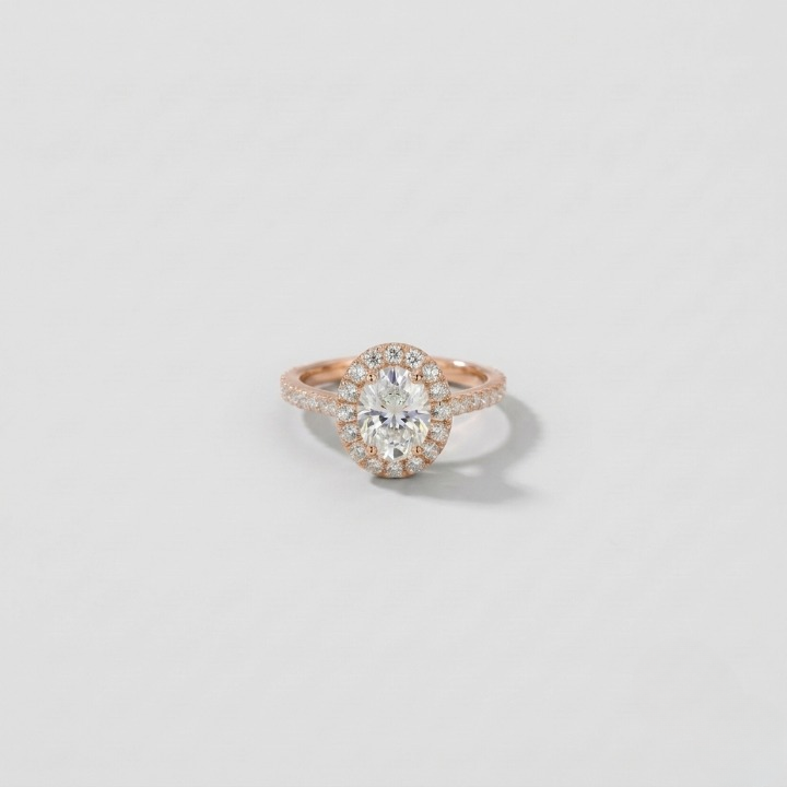 A rose gold halo engagement ring featuring a large oval center stone surrounded by a double halo of small round stones, set on a slim rose gold band, photographed on a light gray background.