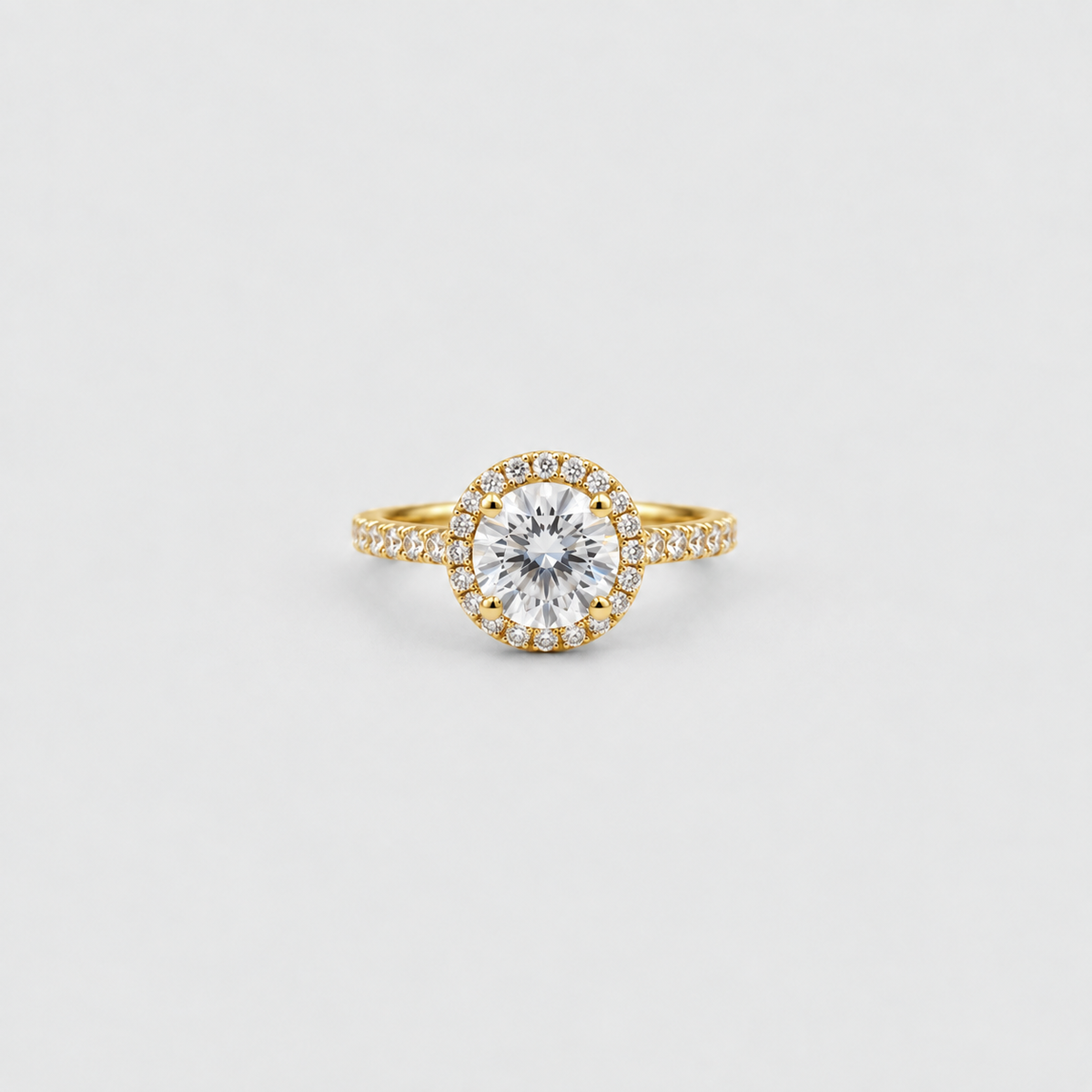 A yellow gold halo ring featuring a round brilliant-cut center stone surrounded by a halo of small pavé-set stones, with a matching pavé-set band, shown on a light gray background.