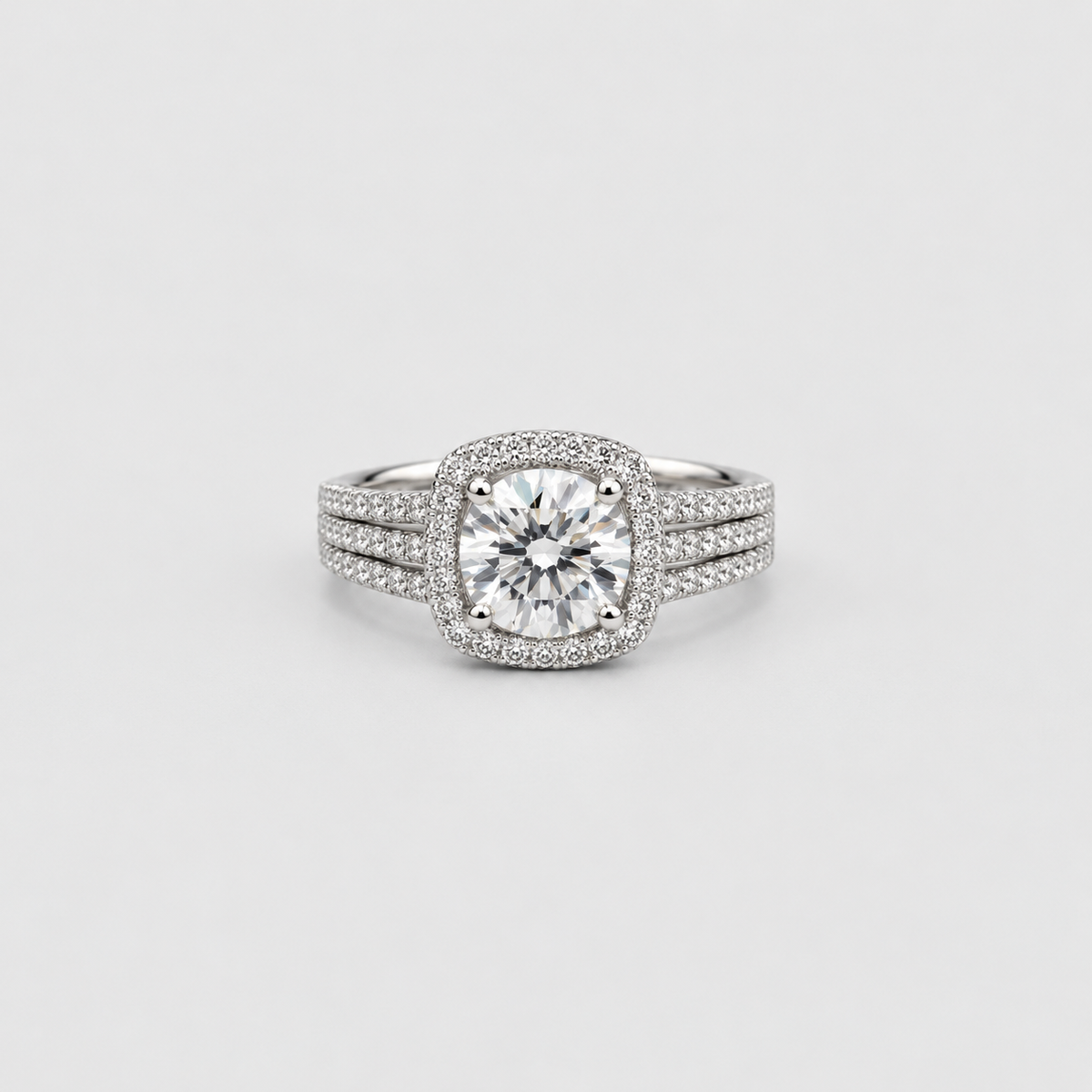 A silver-toned halo ring featuring a round brilliant-cut center stone surrounded by a halo of smaller stones, with a three-stone split band also paved with small diamonds, set against a light gray background.