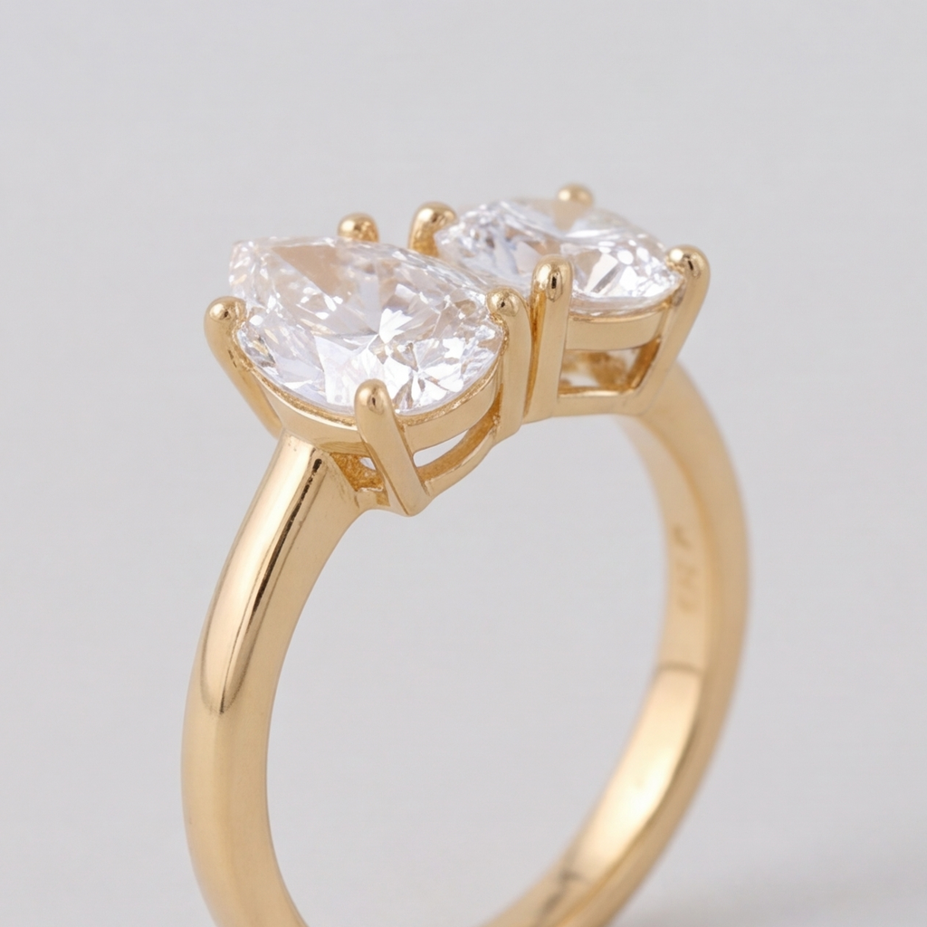 A yellow gold ring featuring two marquise-cut clear gemstones in a prong setting, shown against a neutral light gray background.
