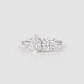 A silver engagement ring featuring a pear-cut diamond on the left and a round-cut diamond on the right, set on a polished silver band against a light gray background.