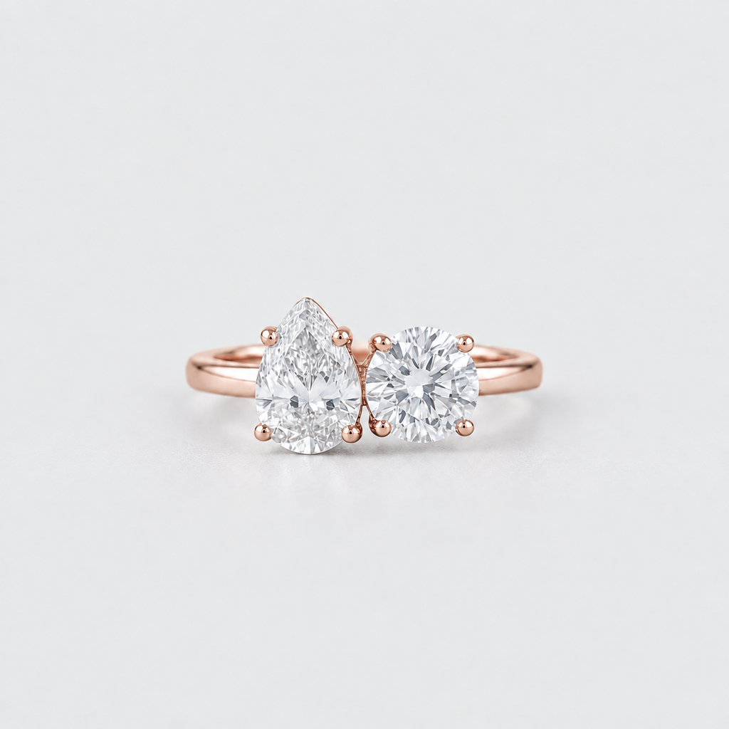 A rose gold engagement ring featuring a pear-cut diamond on the left and a round brilliant-cut diamond on the right, set on a clean white background.
