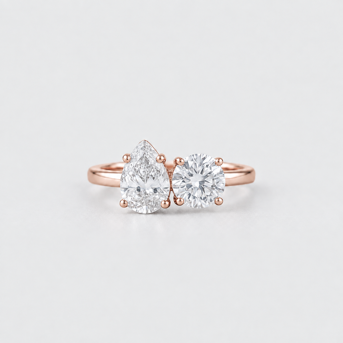 A rose gold engagement ring featuring a pear-cut diamond on the left and a round brilliant-cut diamond on the right, set on a clean white background.