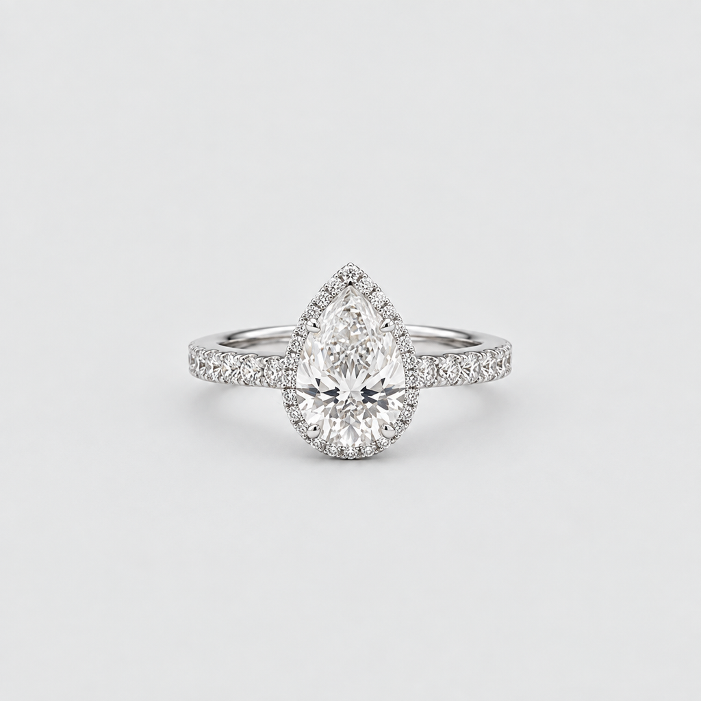A pear-cut diamond halo ring in a silver-toned setting, featuring a halo of small diamonds around a larger pear-shaped center stone, with a diamond-accented band, photographed on a clean light gray background.