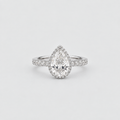 A pear-cut diamond halo ring in a silver-toned setting, featuring a halo of small diamonds around a larger pear-shaped center stone, with a diamond-accented band, photographed on a clean light gray background.