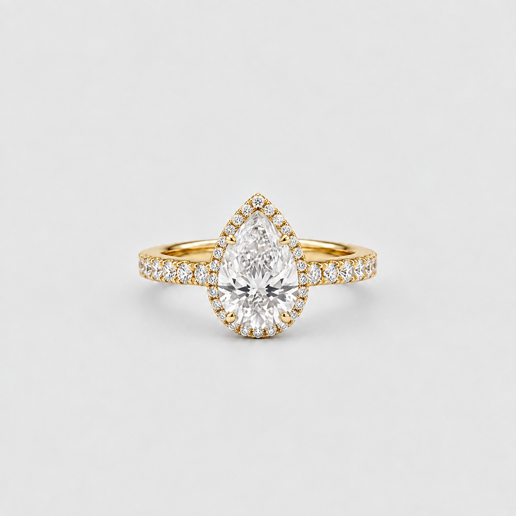 A pear-cut diamond halo ring in yellow gold with pavé diamonds on the band, centered on a light gray background.