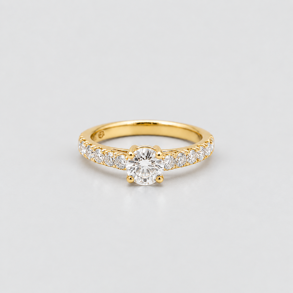 A yellow gold ring featuring a round-cut center stone and a pavé-set row of small clear stones along the band, photographed on a clean light gray background.