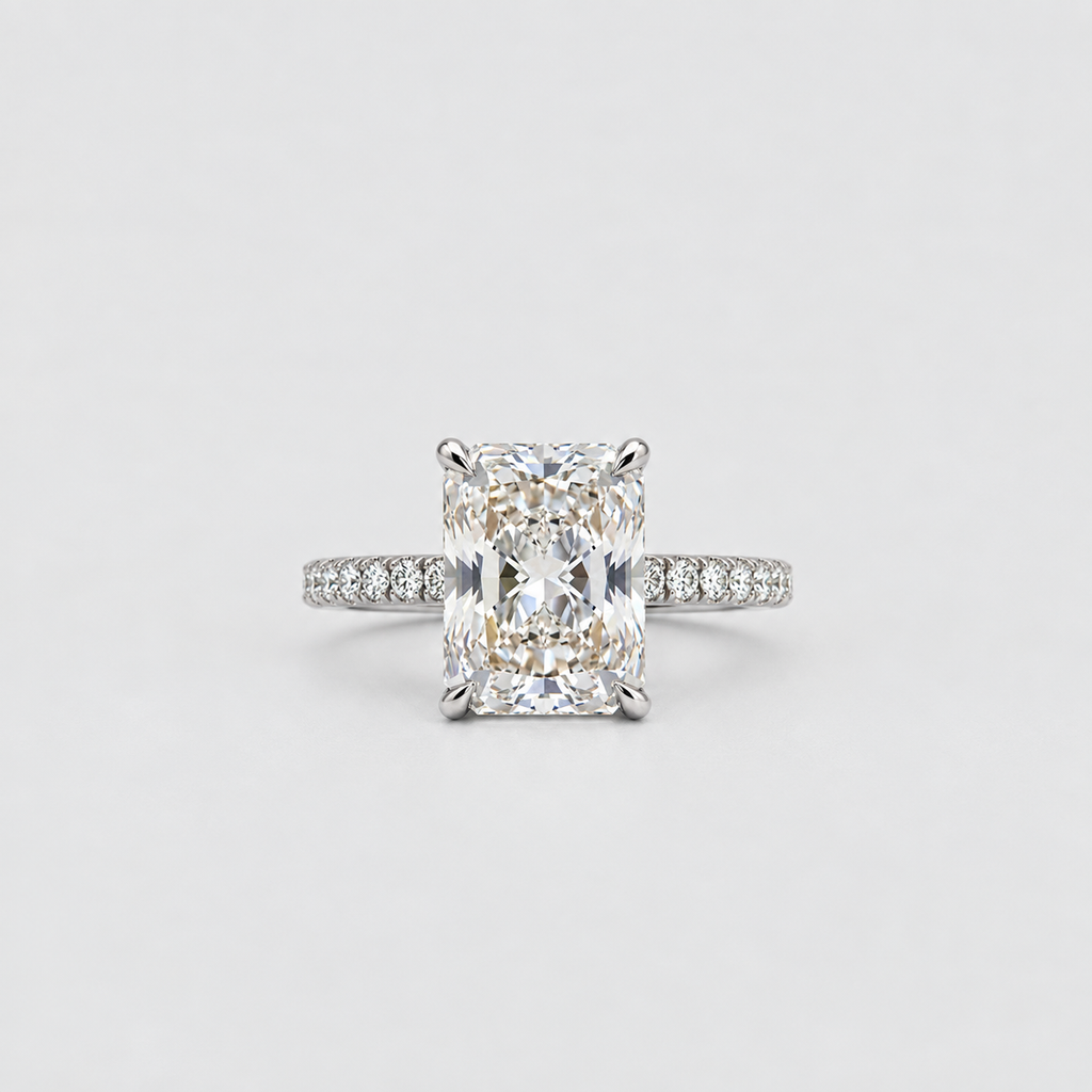 An emerald-cut diamond engagement ring with a pavé band in white gold or platinum, centered on a light gray background.