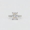 An emerald-cut diamond engagement ring with a pavé band in white gold or platinum, centered on a light gray background.