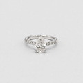 A silver-toned diamond ring featuring a pear-cut center stone and a pavé band with smaller diamonds, set against a plain light gray background.