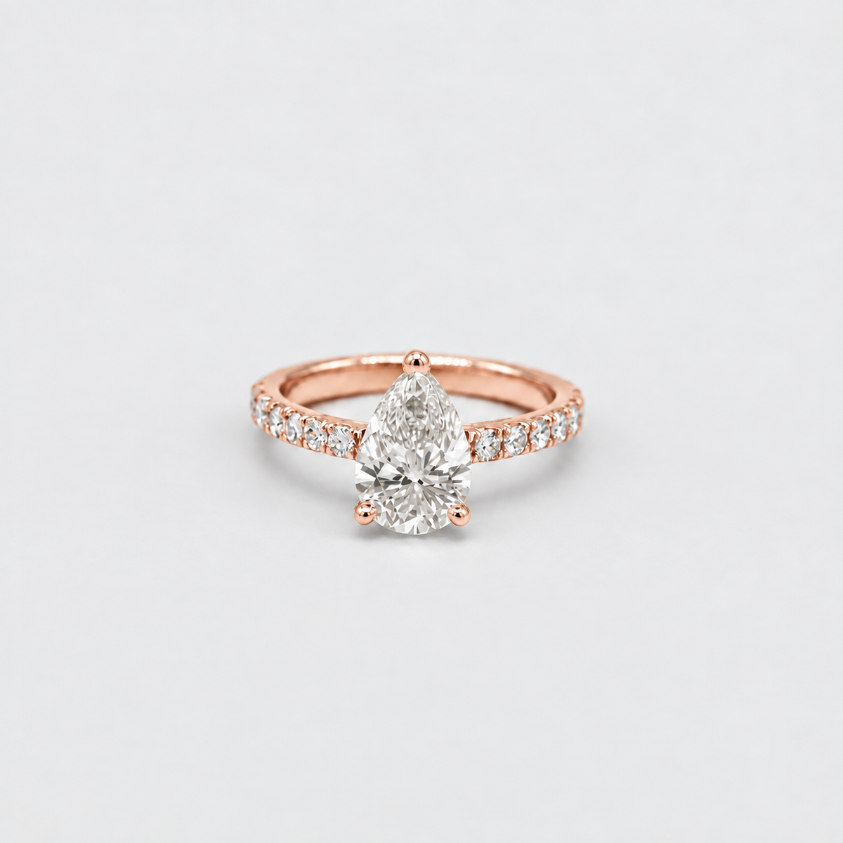A pear-cut diamond engagement ring in rose gold with a pavé-set band, photographed on a clean light gray background.