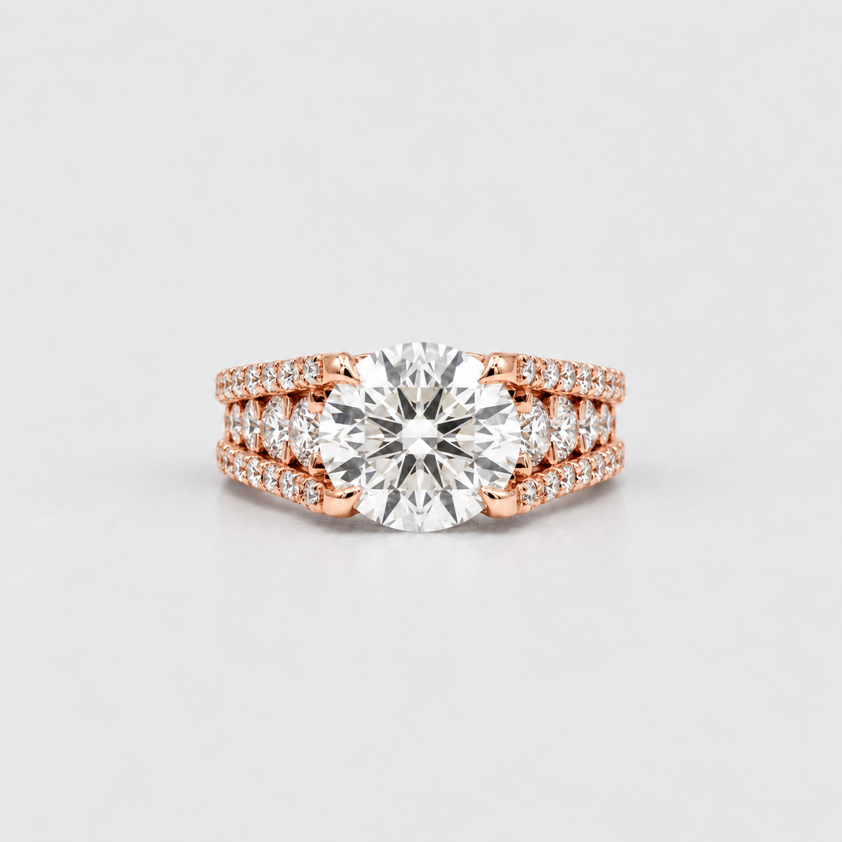 A rose gold engagement ring with a round brilliant-cut center stone and pavé-set side stones, shown on a clean light gray background.