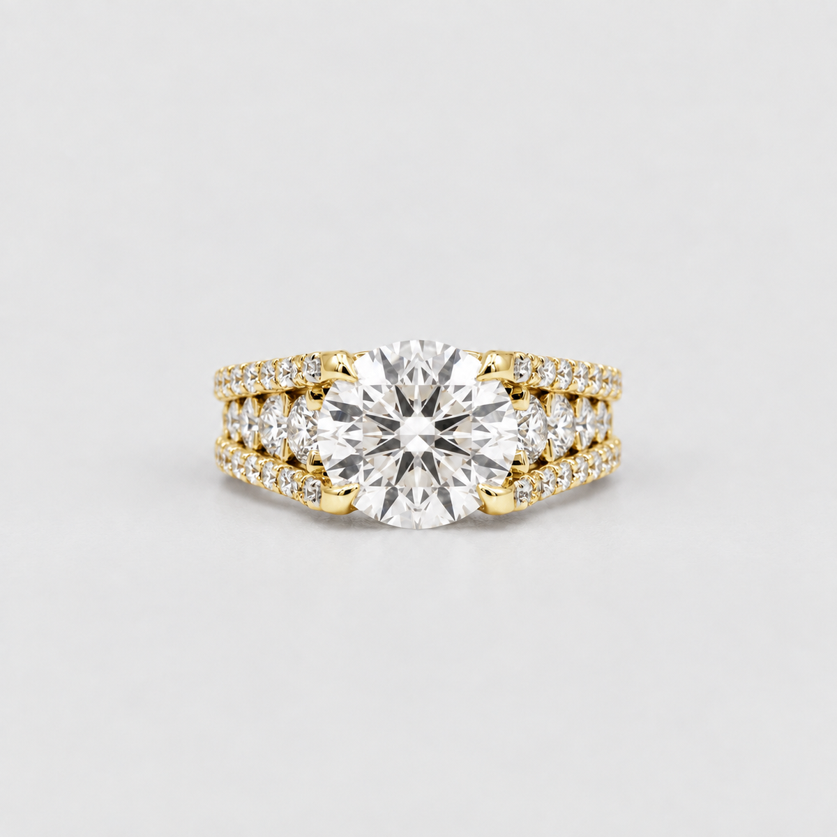 A yellow gold engagement ring set featuring a large round-cut center stone with smaller pavé-set diamonds along the shoulders, photographed on a clean light gray background.