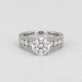 A silver-toned diamond ring with a large round-cut center stone and smaller diamonds set along the shoulders, shown on a light gray background.