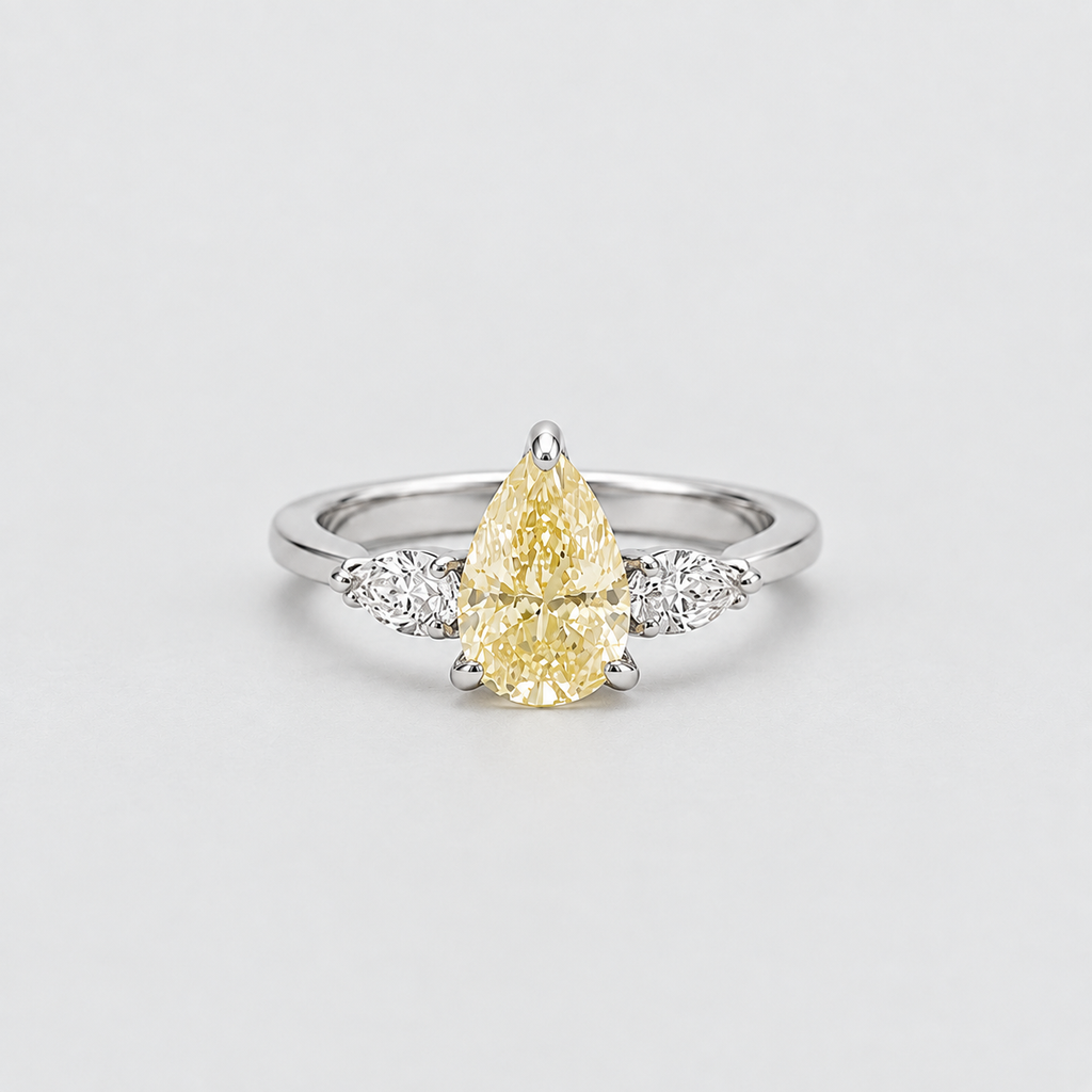 A pear-cut yellow diamond ring with a silver-colored band and small clear accent diamonds on either side, photographed on a clean light gray background.
