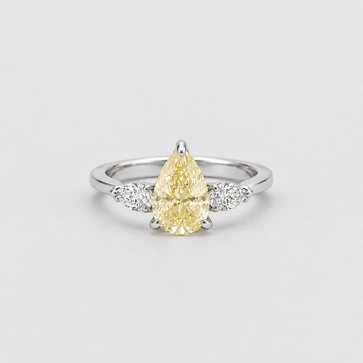 A pear-cut yellow diamond ring with a silver-colored band and small clear accent diamonds on either side, photographed on a clean light gray background.