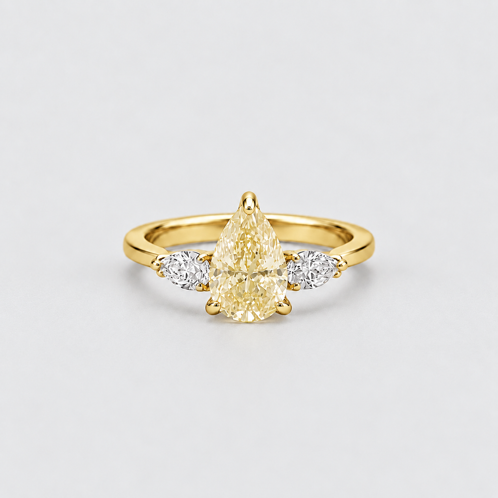 A yellow gold ring featuring a pear-cut center stone and two marquise-cut side stones, photographed on a clean light gray background.
