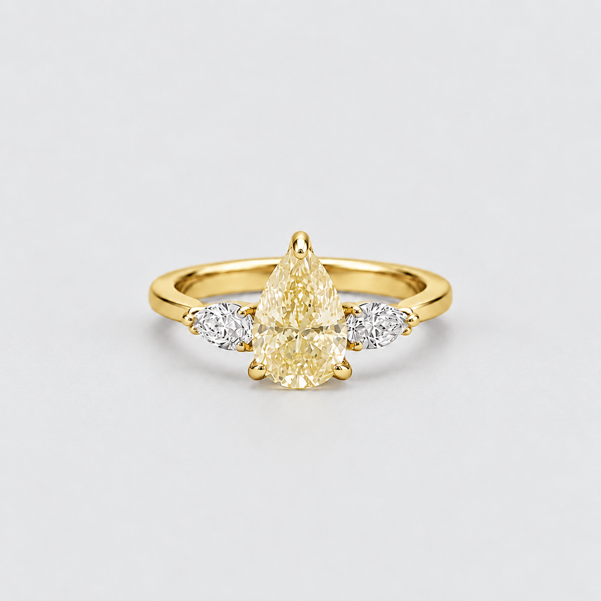 A yellow gold ring featuring a pear-cut center stone and two marquise-cut side stones, photographed on a clean light gray background.