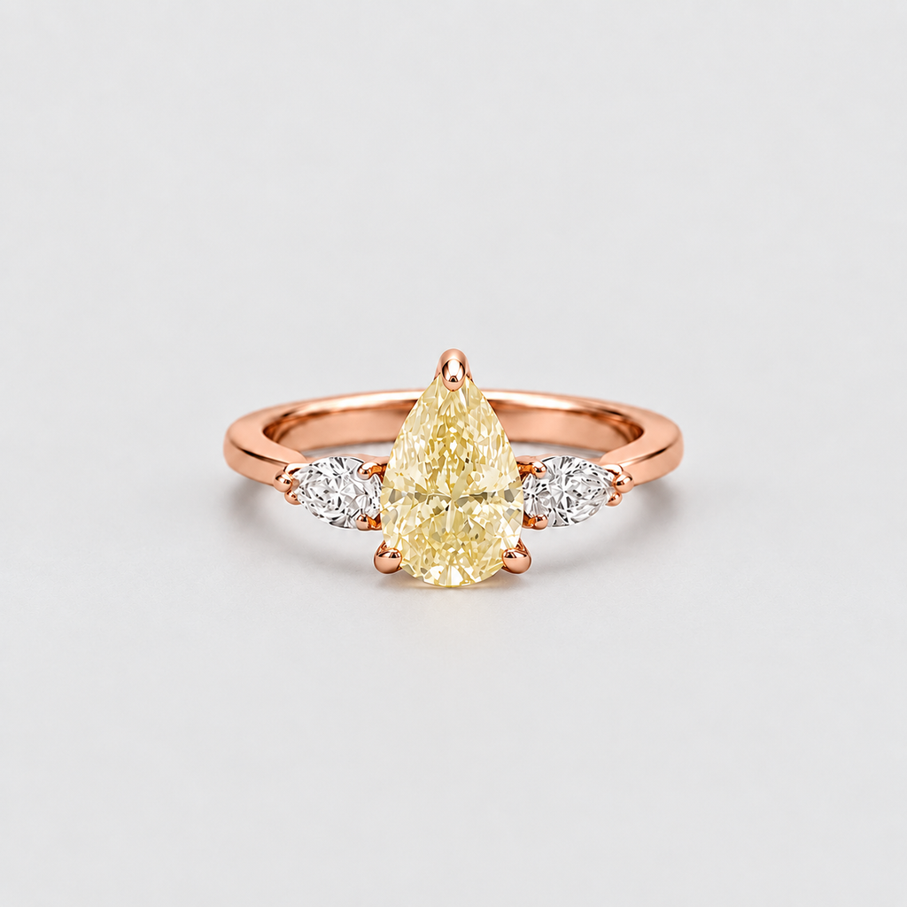 A rose gold ring featuring a pear-cut yellow center stone flanked by two small round clear stones, set against a clean light gray background.