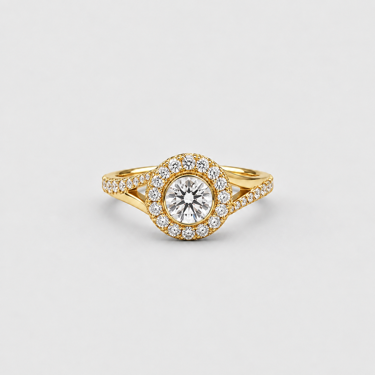 A yellow gold ring featuring a round-cut center stone surrounded by a halo of smaller clear stones, with a shank paved with additional stones, set against a light gray background.