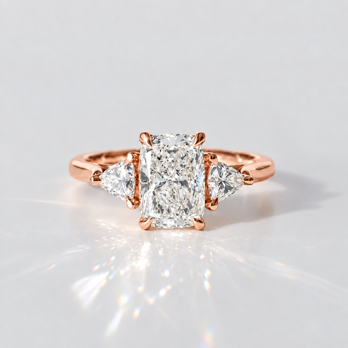 A rose gold ring featuring a large rectangular center diamond flanked by two smaller pear-cut diamonds, set against a clean white background with a soft reflection.