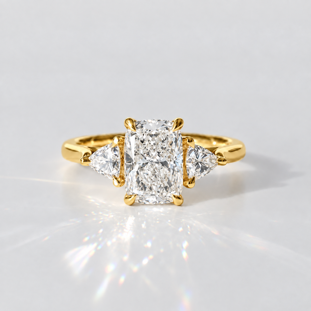 A yellow gold ring featuring a large rectangular radiant-cut diamond center stone with two smaller marquise-cut diamonds on either side, set against a clean white background with a soft reflection.