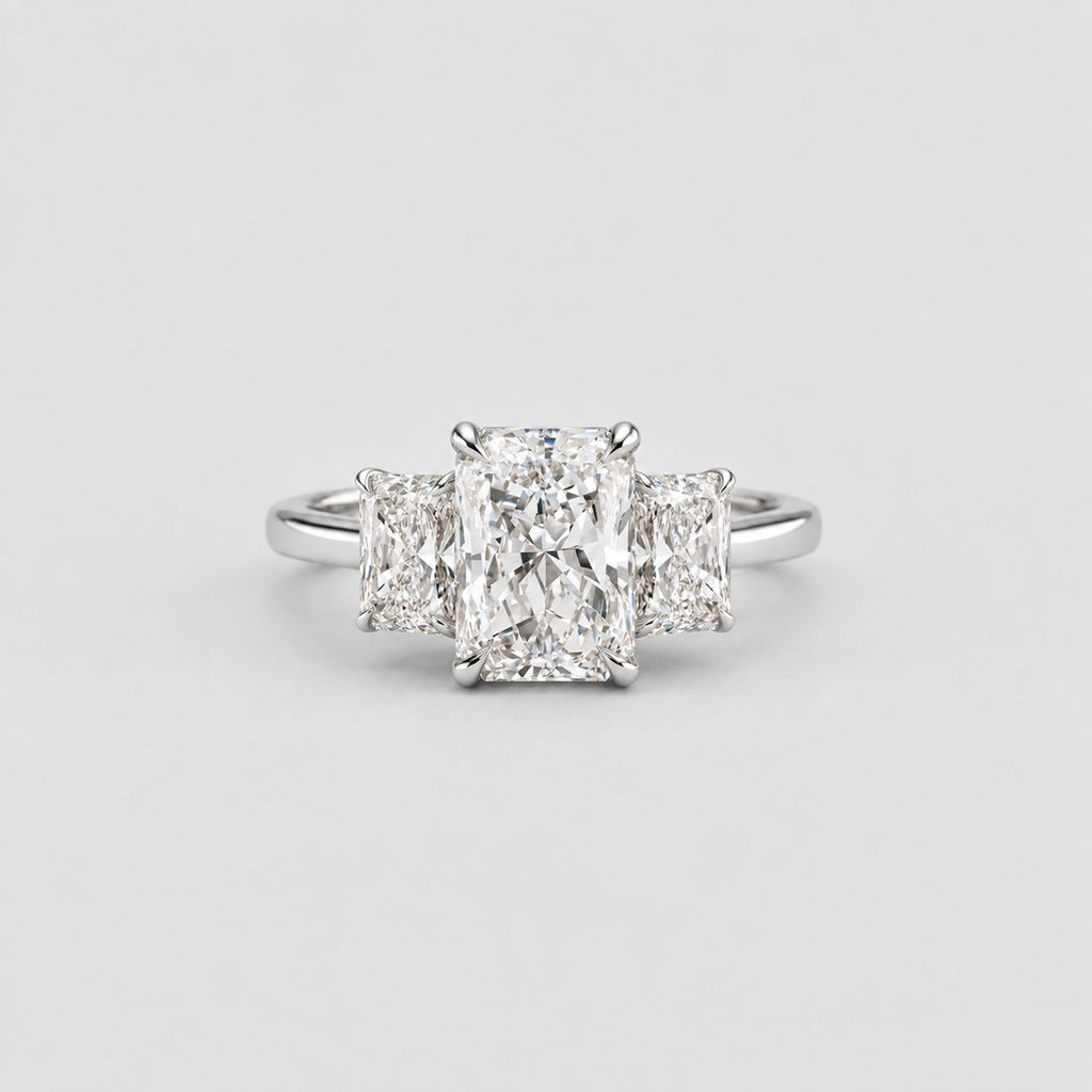 A three-stone diamond engagement ring with a central radiant-cut diamond flanked by two smaller cushion-cut diamonds on a polished silver-colored band, set against a light gray background.