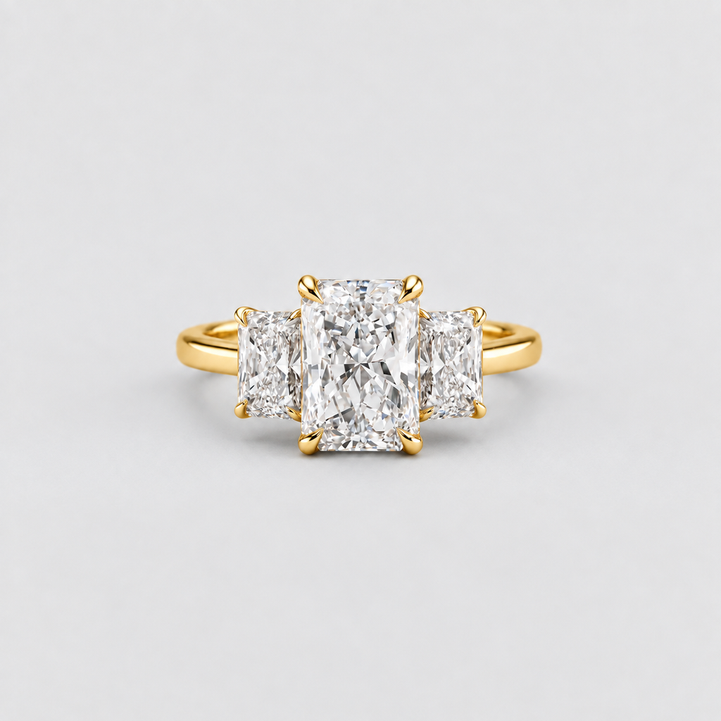 A yellow gold three-stone ring featuring a large center radiant-cut diamond flanked by two smaller round brilliant-cut diamonds, set against a clean light gray background.