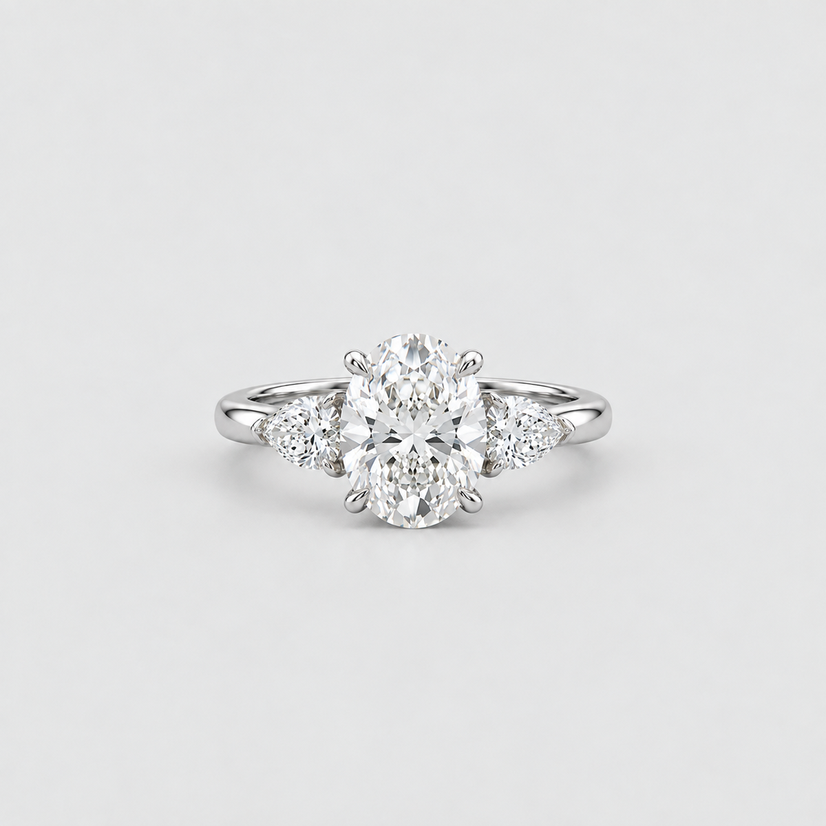 A silver diamond ring with a large oval center stone and three smaller round diamonds flanking it on a clean light gray background.