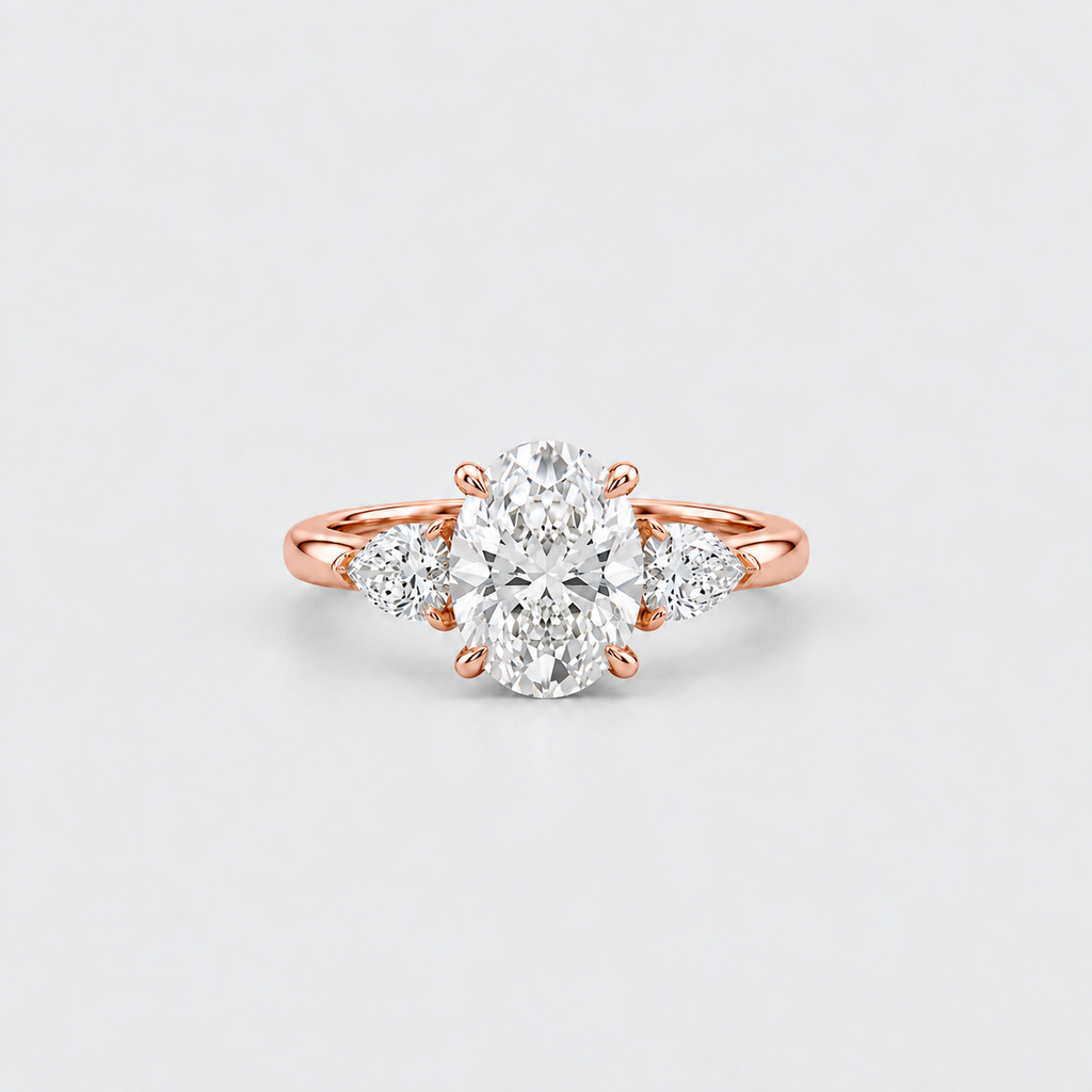 A rose gold engagement ring featuring a large oval center diamond flanked by two round side diamonds, set against a clean light gray background.