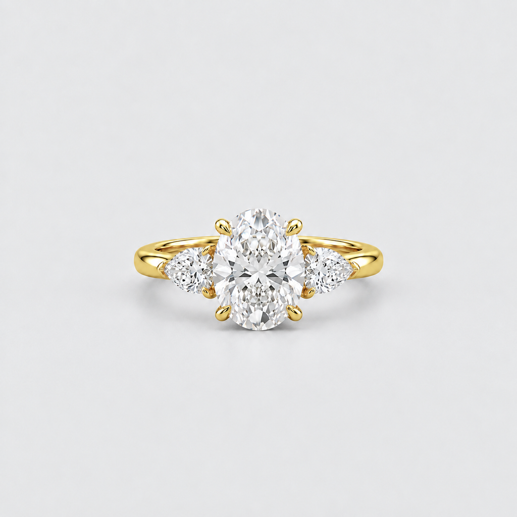 A yellow gold three-stone diamond ring with a large oval center stone and two smaller round side stones, photographed on a clean light gray background.