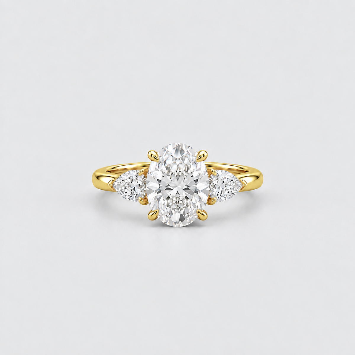 A yellow gold three-stone diamond ring with a large oval center stone and two smaller round side stones, photographed on a clean light gray background.