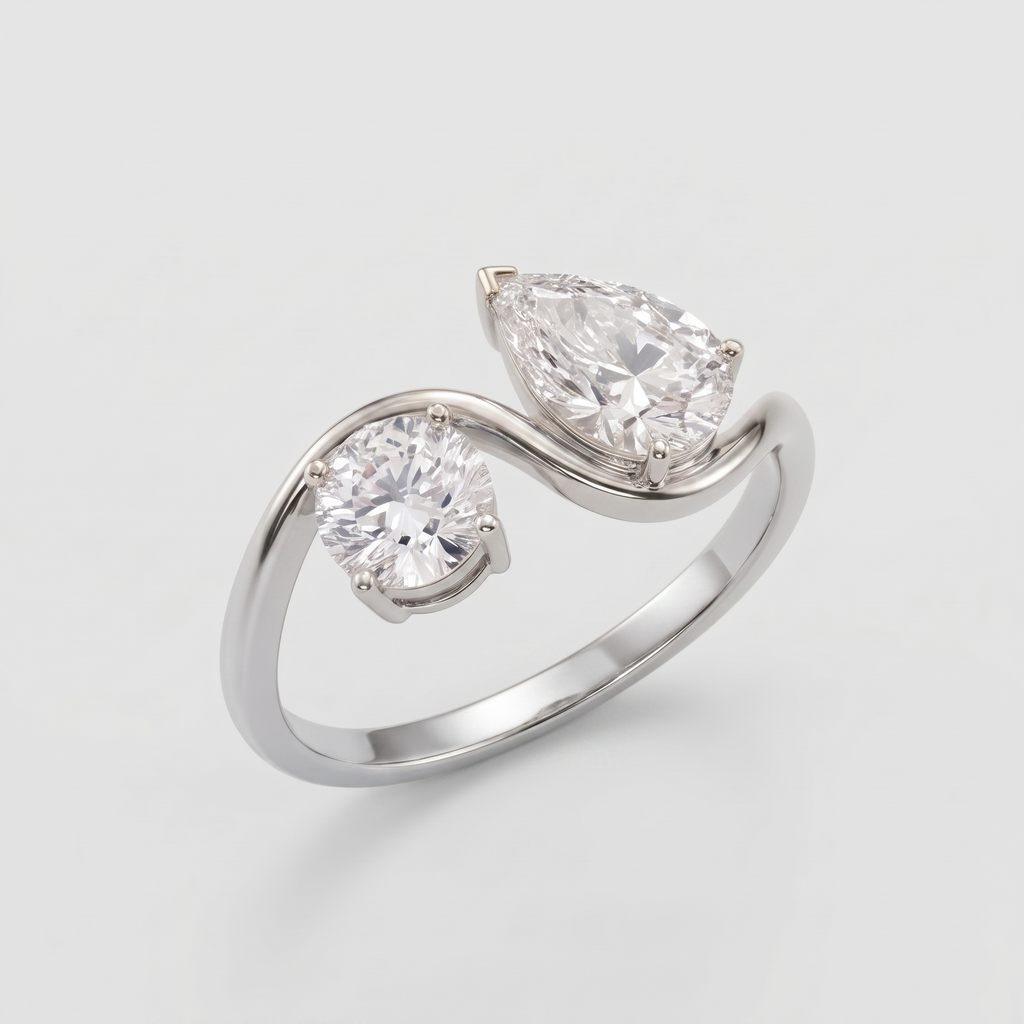 A silver-tone split-shank ring featuring one round brilliant-cut diamond and one pear-cut diamond in prong settings, shown on a light gray background.