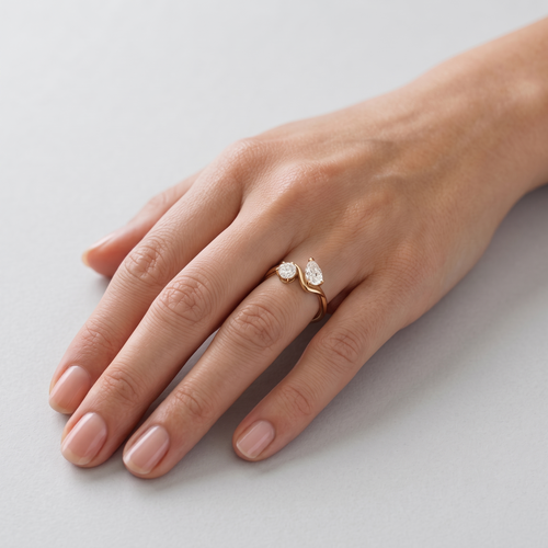 A close-up of a person's hand wearing a delicate gold ring with two small clear gemstones on a light gray background.