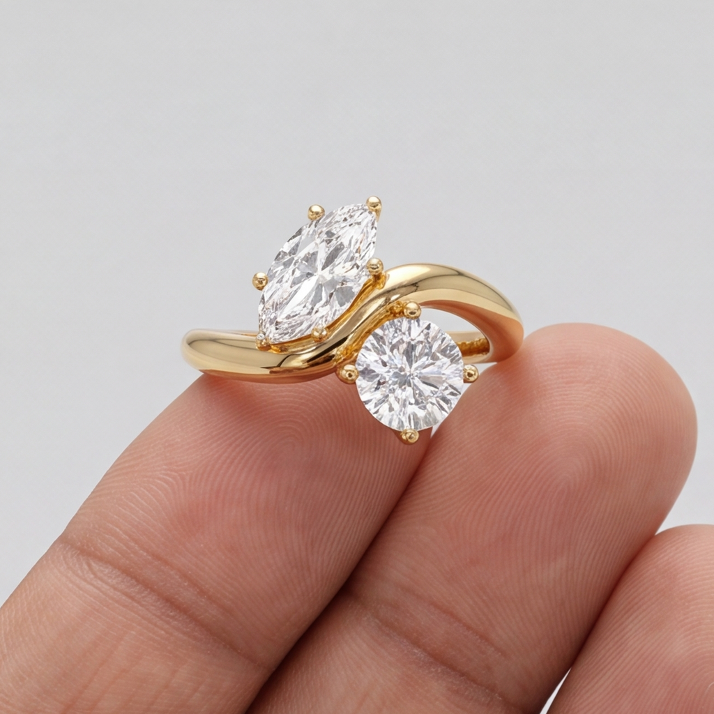 A gold ring with a marquise-cut clear gemstone and a round brilliant-cut clear gemstone, shown resting on a person's fingers against a light gray background.