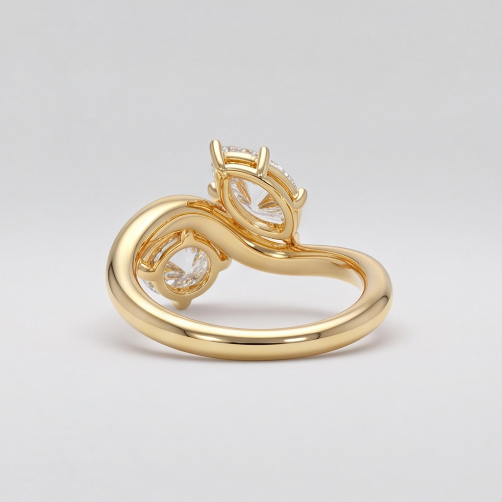 A gold ring with a sculptural, flowing band and a central cluster of clear gemstones, photographed on a neutral light gray background.