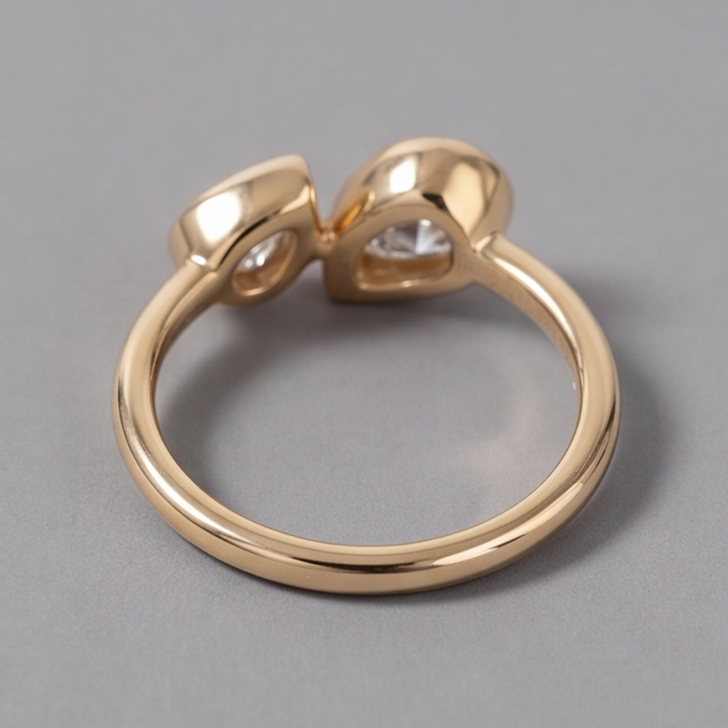 A polished yellow gold ring with a unique double-heart design and small clear gemstones, shown on a neutral gray background.