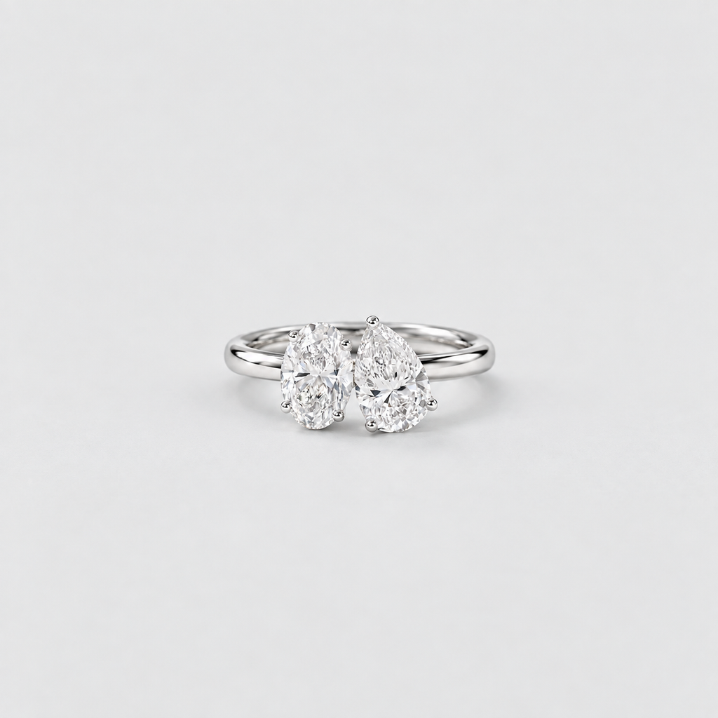 A silver double diamond ring with two pear-cut diamonds in a three-prong setting, shown on a light gray background.