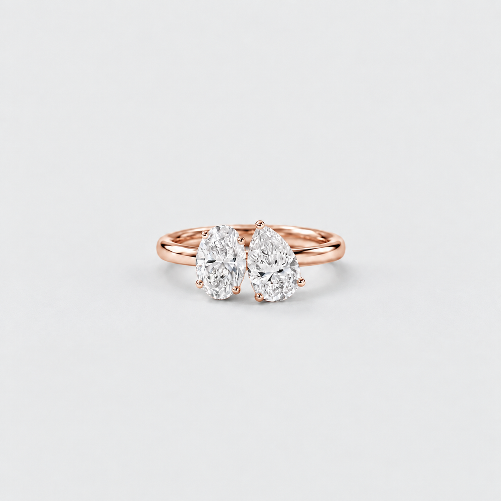 A rose gold double ring featuring two pear-cut diamonds in a prong setting, centered on a light gray background.