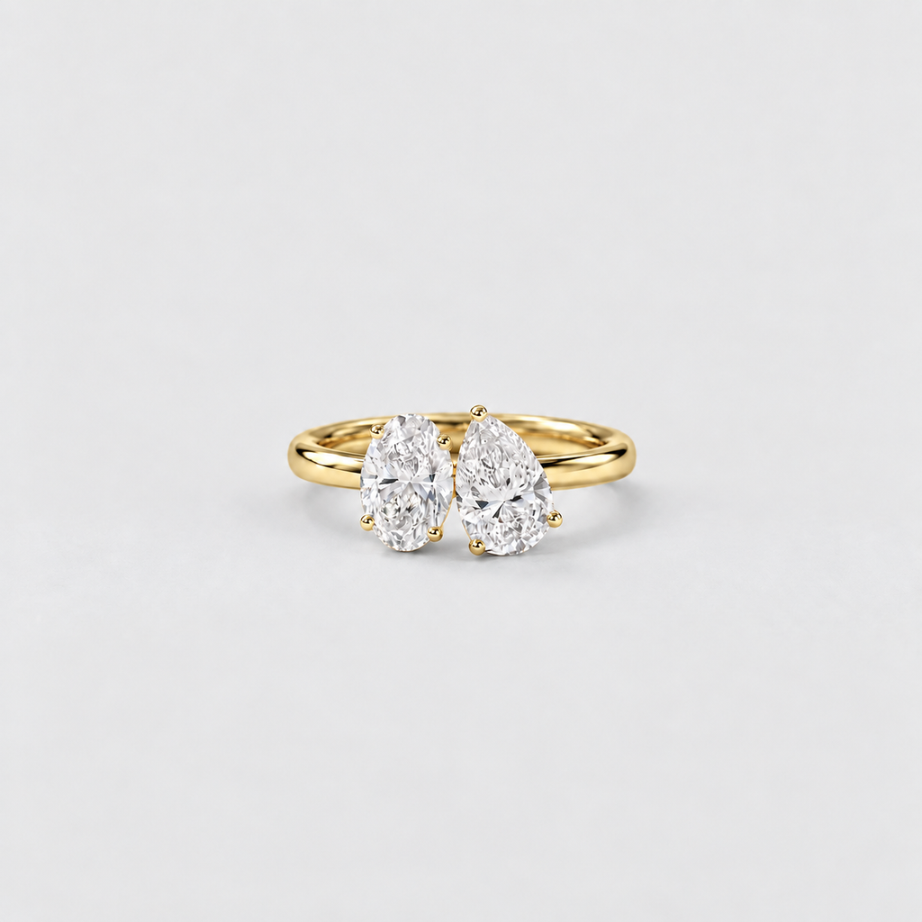 A yellow gold ring featuring two pear-cut diamonds in a side-by-side setting, photographed on a clean, light gray background.