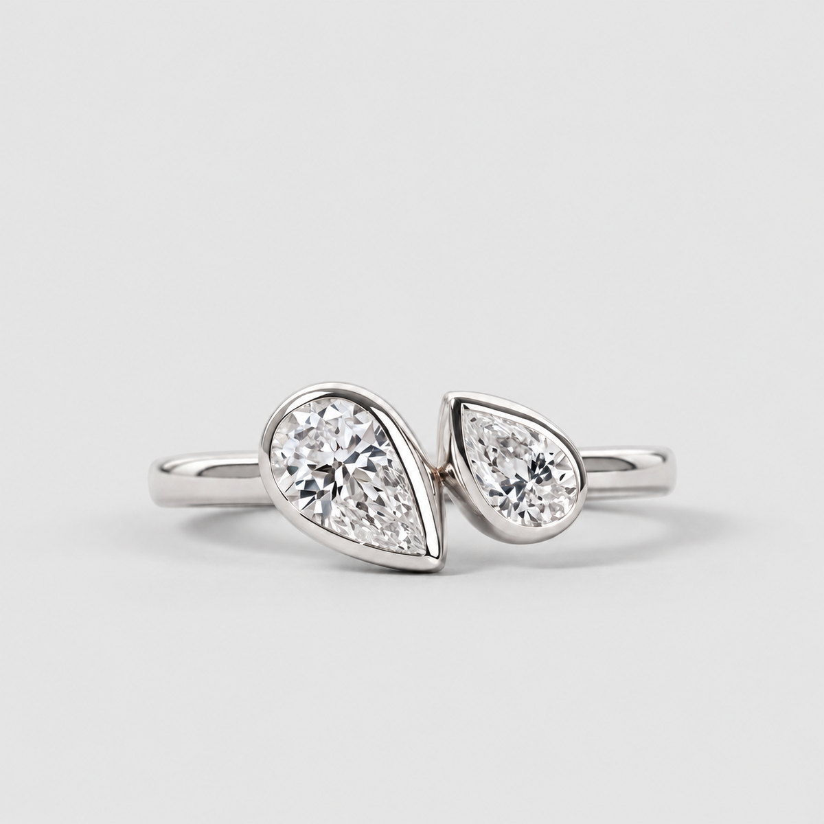 A silver ring featuring two pear-cut diamonds set in a split design, photographed on a clean light gray background.