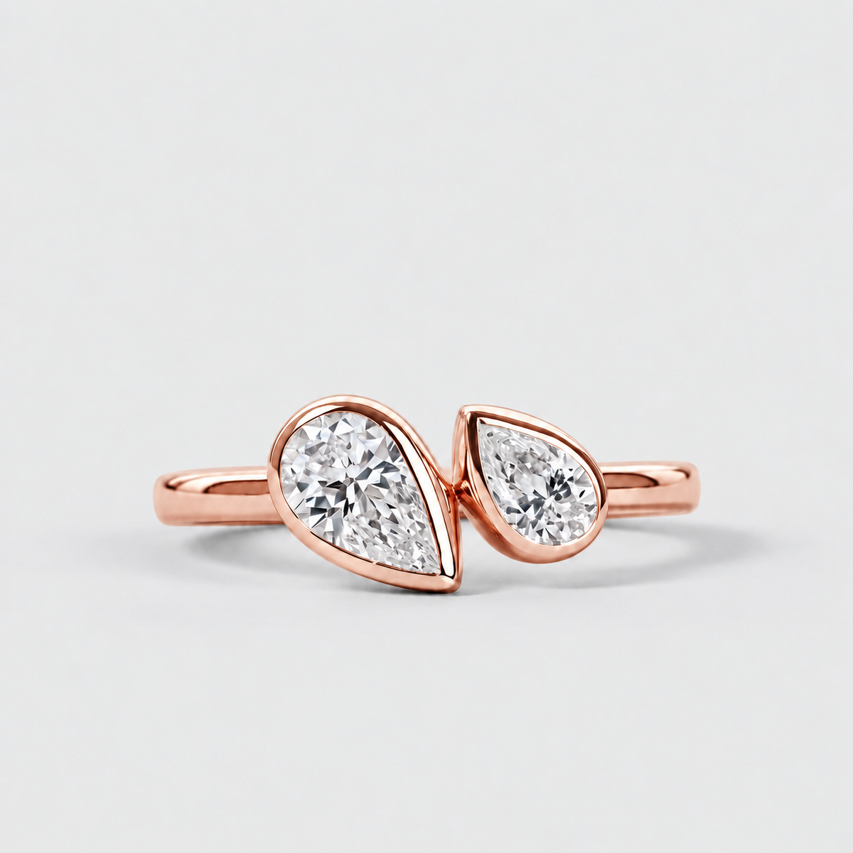 A rose gold ring featuring two pear-cut clear gemstones in a split design, set on a clean light gray background.