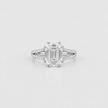 An emerald-cut diamond engagement ring with a silver-toned diamond-accented band, centered on a light gray background.