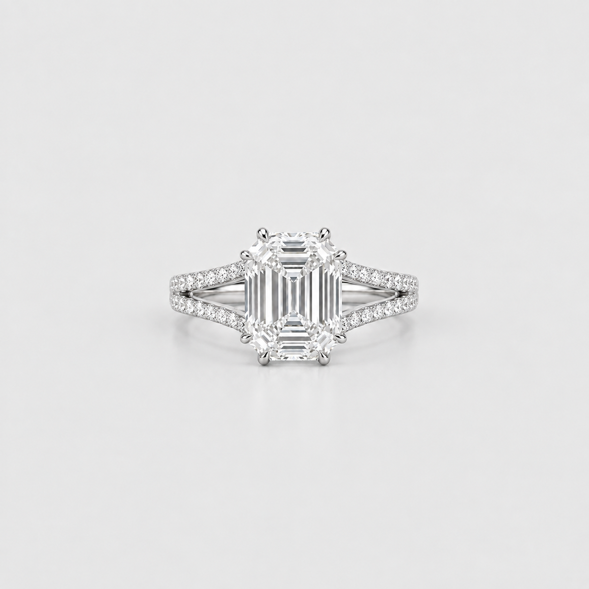 An emerald-cut diamond engagement ring with a silver-toned diamond-accented band, centered on a light gray background.