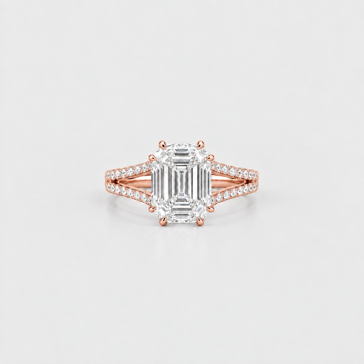 A rose gold engagement ring featuring a large emerald-cut diamond center stone and pavé-set diamonds along a split shank, shown on a clean light gray background.