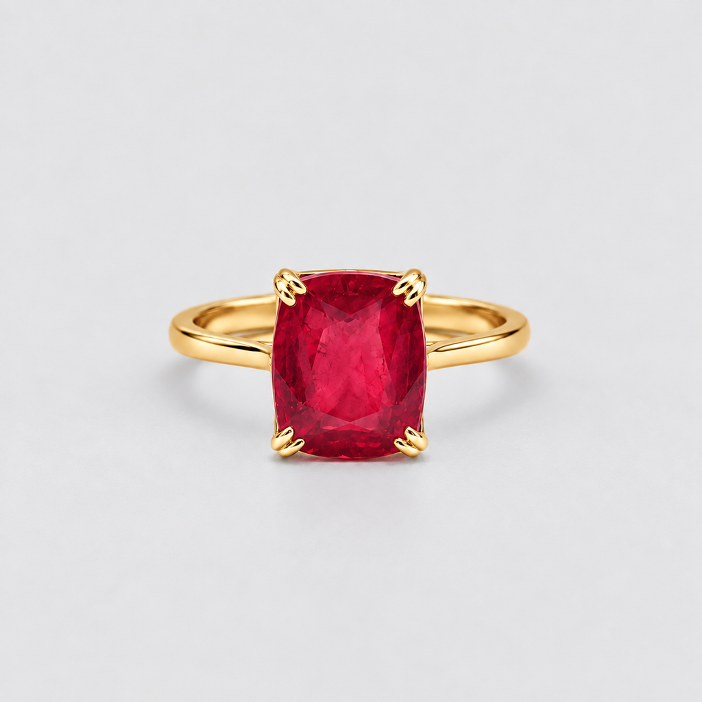 A yellow gold ring featuring a cushion-cut, faceted red gemstone in a four-prong setting, shown against a neutral light gray background.