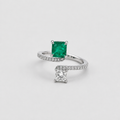 A silver-tone ring featuring a square-cut green emerald gemstone and a separate princess-cut clear gemstone, both set on a pavé-set silver band, photographed on a light gray background.