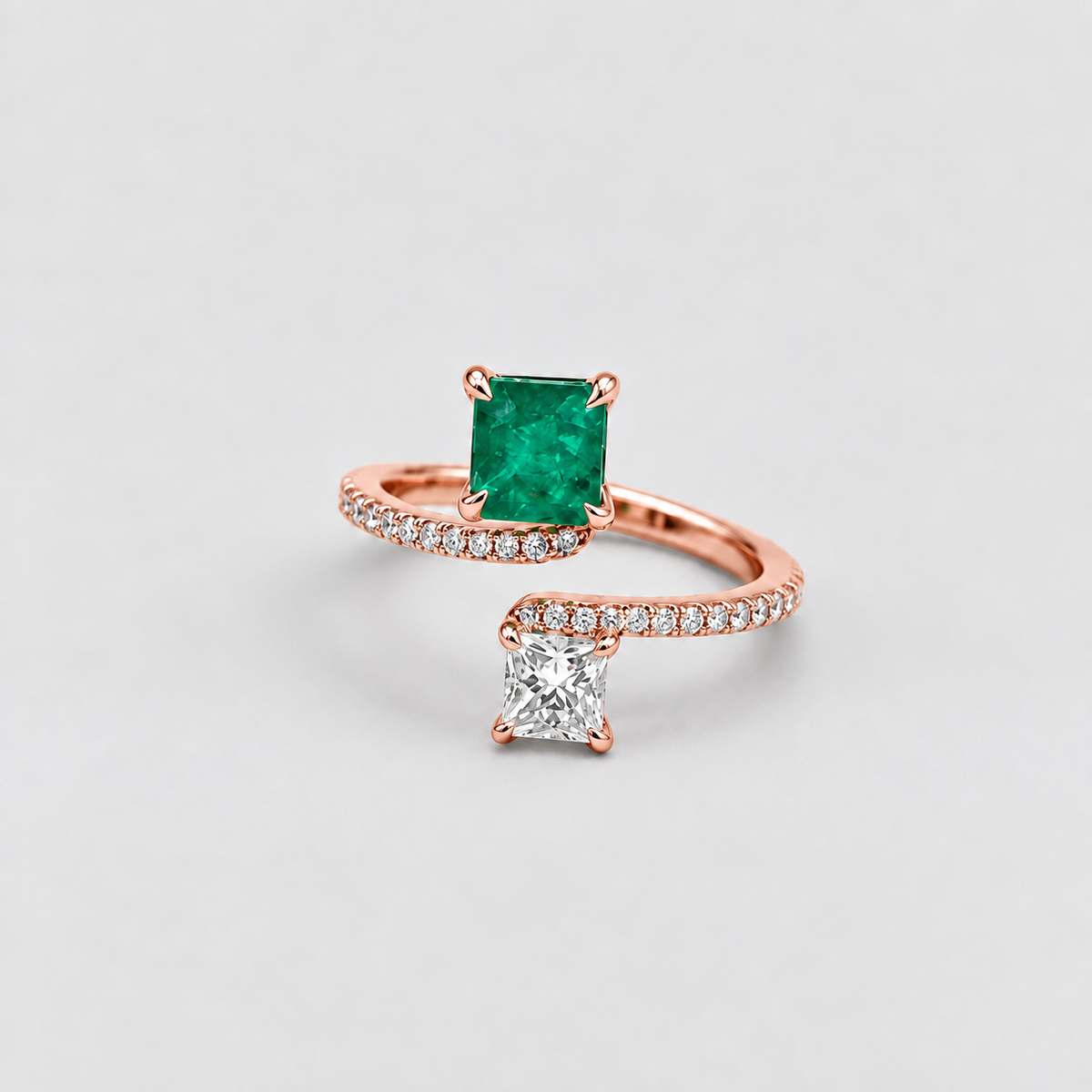 A rose gold ring with a square-cut green emerald gemstone and a second rose gold ring with a square-cut clear diamond, displayed on a light gray background.