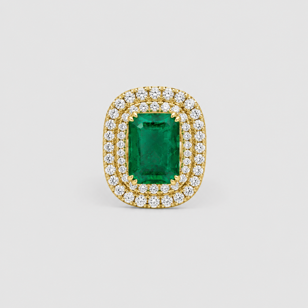 A yellow gold ring featuring a rectangular emerald-cut green gemstone surrounded by a double halo of round brilliant-cut clear stones, set against a neutral light gray background.