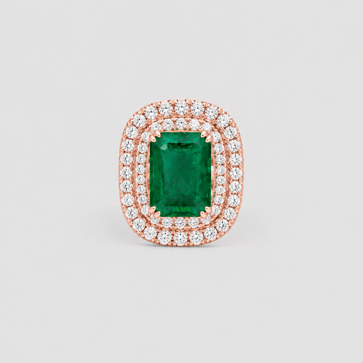 A rose gold ring featuring a rectangular emerald-cut green emerald center stone surrounded by a double halo of round brilliant-cut diamonds, set against a neutral light gray background.